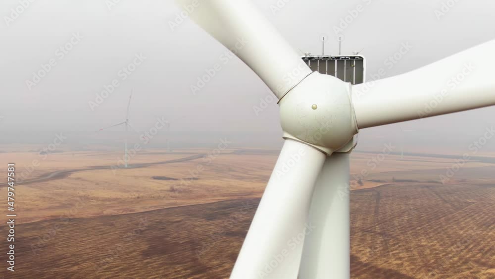 Wind mill rotor close up shot, aerial view. Zoom out from turbine tower with meteo station mechanisms. Wind turbine farm on the background.