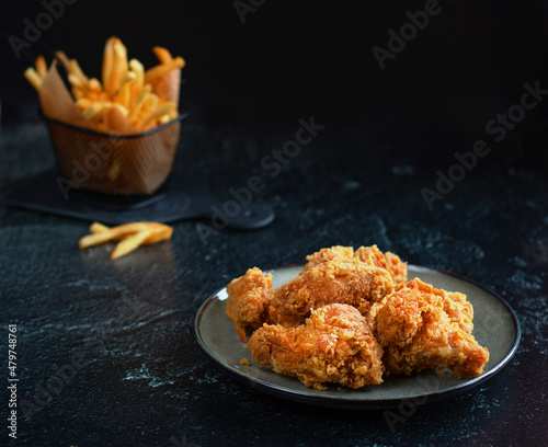 Spicy fried chicken wings, breaded on a ceramic plate. There are fries in the background. Photo on a dark background. Low key. Minimalism. Selective focus.
