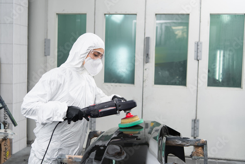 Workwoman in protective suit polishing car part in service.