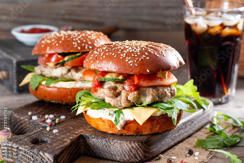Tasty grilled homemade burgers with beef, tomato, cheese and arugula on wooden background. Fast food and junk food concept.