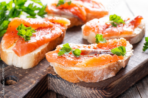 Slices of fresh baguette with butter and salmon served on wooden board on wood table