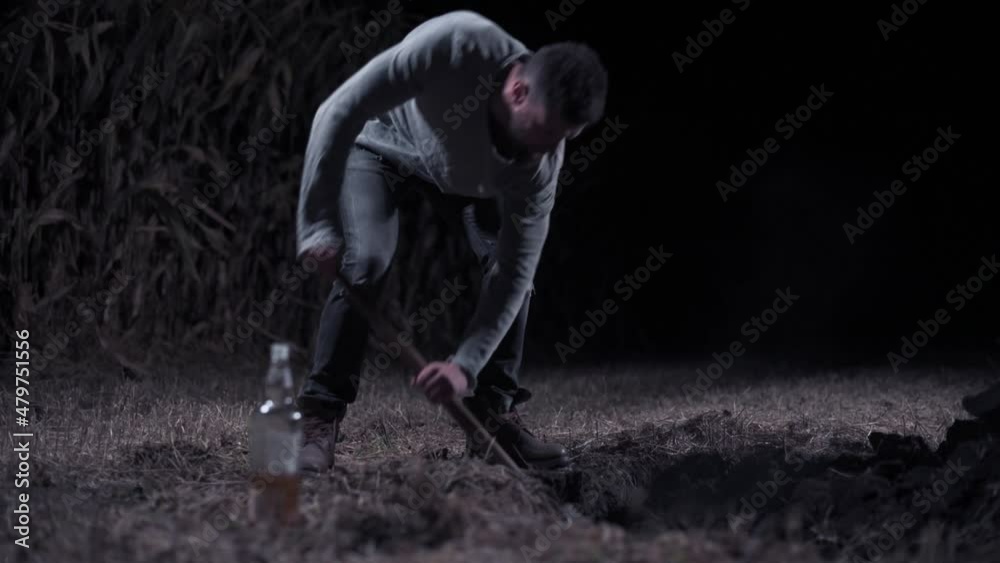 Criminal digs hole at night Young scary man digs hole in field. Long shot.