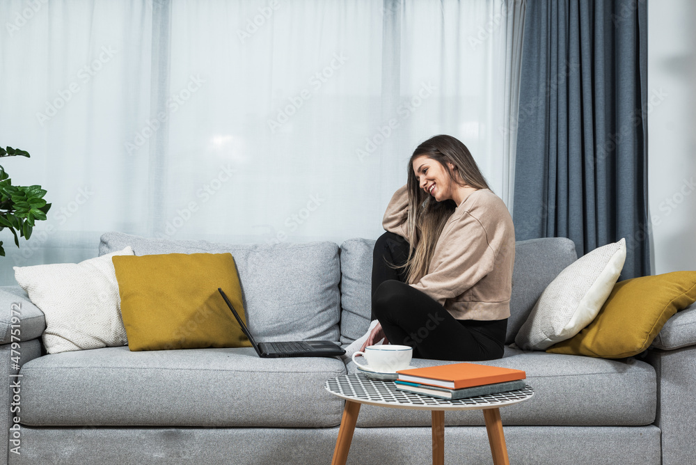 Young smiling happy woman online dating from home on her laptop computer. Carefree female college student talking on video call with her boyfriend who is on another college campus.