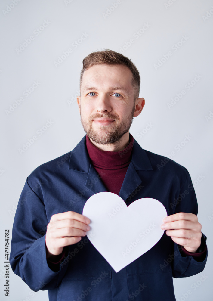 St. Valentine's Day symbols: portrait of young bearded male construction worker standing by the wall holding white paper heart shape. Romance or relationships concept. High quality image St. Valentine's Day symbols: portrait of young bearded male construction worker standing by the wall holding white paper heart shape. Romance or relationships concept. High quality image