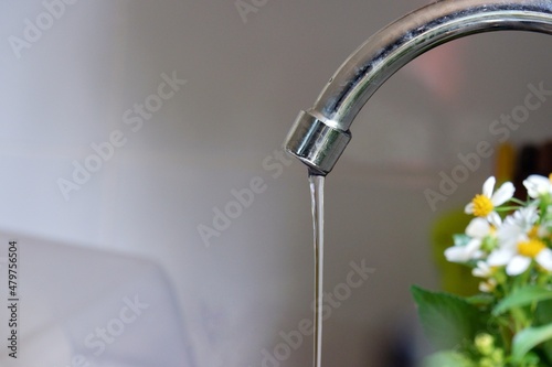 In selective focus water running from a metal faucet in kitchen area with wall background 