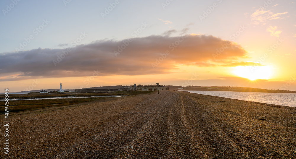 Fototapeta premium The long pebble spit at sunrise leading to Hurst Castle English heritage military fort and Hurst Point Lighthouse in the distance. No people. Milford on Sea, Lymington, England