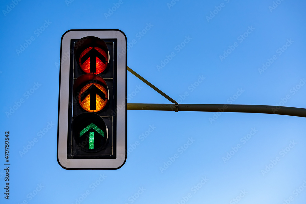 German traffic lights “Ampel“ with all three flashlights shining  simultaneously isolated on blue sky. Red, orange or yellow, green light  with arrows indicating “straight ahead“, hanging above crossing Stock-bilde  | Adobe Stock