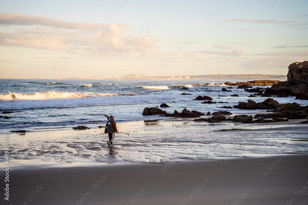 A man with fishing equipment walking on the beach with beautiful rocks formations, Sines, Portugal A man with fishing equipment walking on the beach with beautiful rocks formations, Sines, Portugal