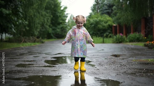 A child plays outside on a rainy day. A girl runs through the puddles in rubber yellow boots and a bright raincoat