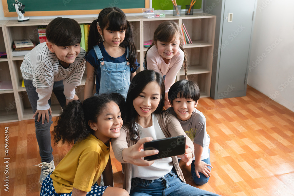 Diverse school kids and Asian woman Teacher taking selfie with mobile phone or smartphone. Diverse school kids and Asian woman Teacher taking selfie with mobile phone or smartphone.