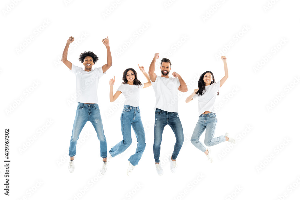 excited multiethnic friends in jeans looking at camera while levitating on white.