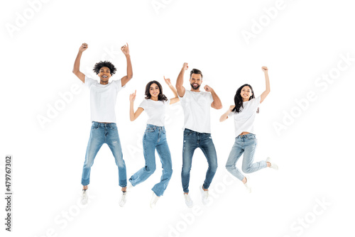 excited multiethnic friends in jeans looking at camera while levitating on white.