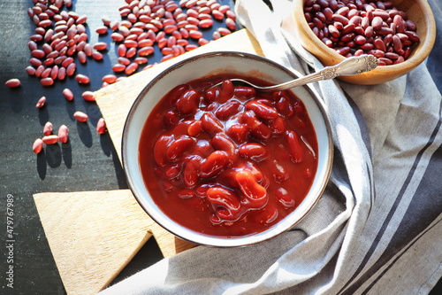 Raw and canned red kidney chilli beans in bowl on a rustic wooden table