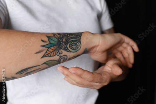 Woman applying cream on her arm with tattoos against black background, closeup