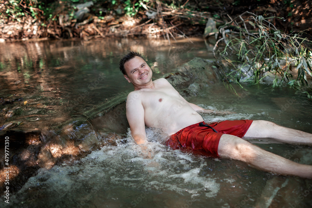Fototapeta premium Happy middle aged man resting in stream canyon river in the mountains, nature pool. Cold water, hardening and natural spa procedure, wildlife and green tourism, active healthy lifestyle, summertime