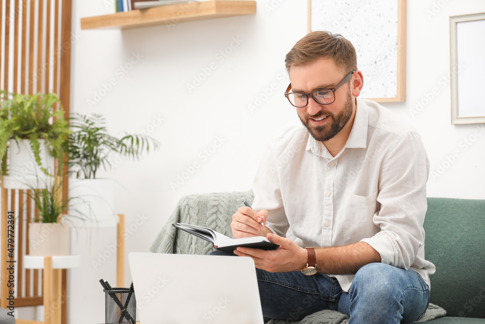 Fototapeta premium Young man working with notebook and laptop at home, space for text