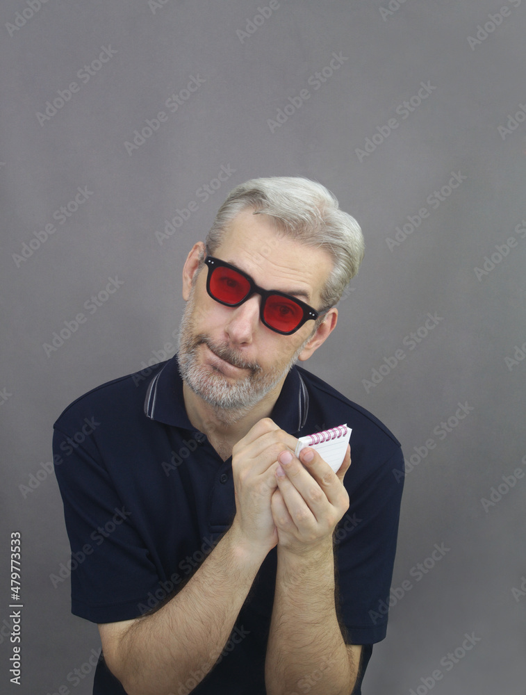 Middle age man with gray hair and beard in red sunglasses writing in notebook on gray background Middle age man with gray hair and beard in red sunglasses writing in notebook on gray background