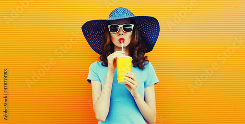 Colorful portrait of beautiful young woman drinking a fresh juice wearing a summer hat an orange background