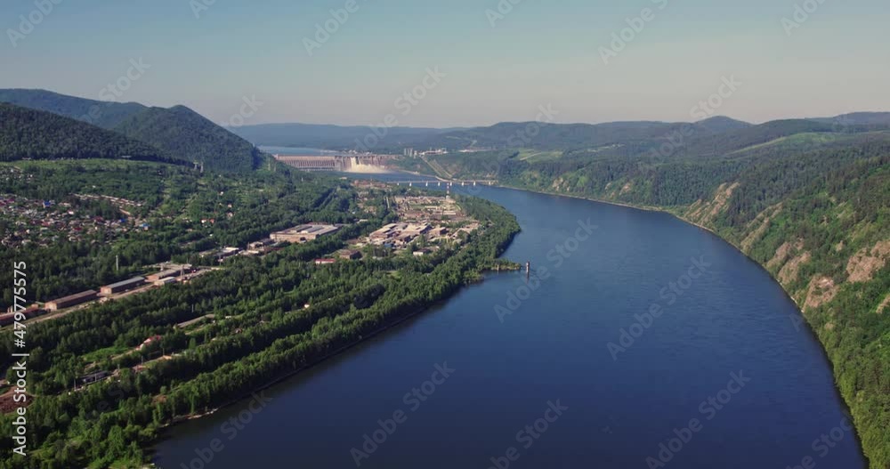 Flying a drone along a wide river and mountains, a hydroelectric power plant in the background. The height of the bird's flight. Flying a drone along a wide river and mountains, a hydroelectric power plant in the background. The height of the bird's flight.