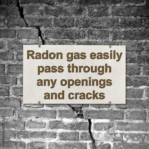 A cracked brick wall with warning message abaut radon gas escaping through cracks and openings - concept image photo
