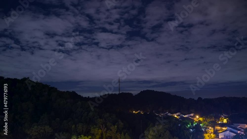 A very stunning night skies with partial clouds with airplane chemtrails sky over a forest hill with 5G Communication tower on top.