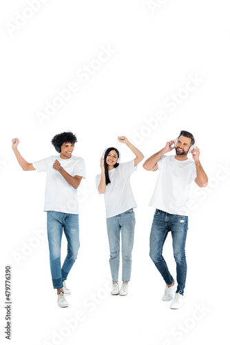 full length view of interracial men and asian woman dancing in headphones on white.