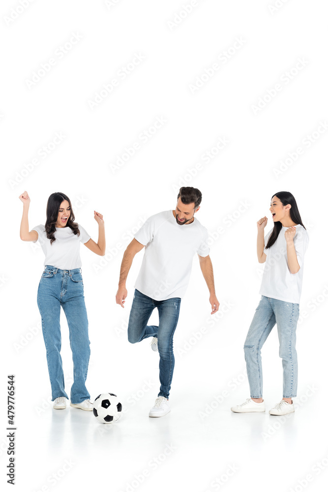excited interracial women showing win gesture near man playing football on white. excited interracial women showing win gesture near man playing football on white.
