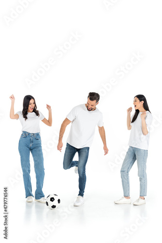 excited interracial women showing win gesture near man playing football on white.