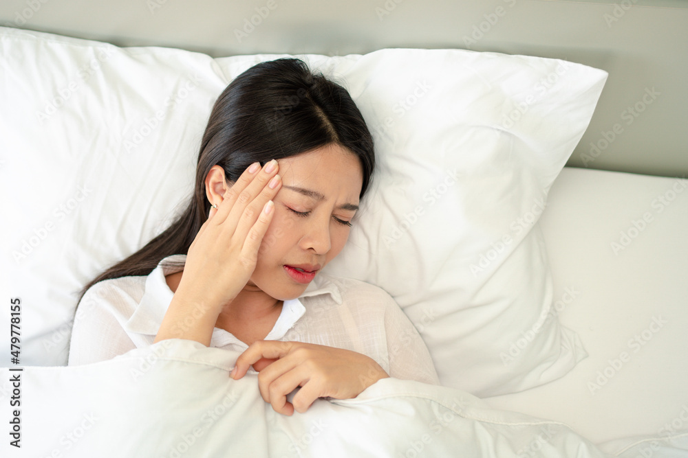 Unhappy exhausted woman closed eyes lying in bed cause of Headache, sore throat and tired, Concept of recuperation from illness, feeling unwell and healthcare.