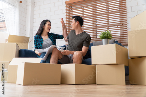 Smiling young Asian happy couple hold blueprint for home decoration ideas at moving day in their new home after buying real estate. Concept of starting a new life for a newly married couple.