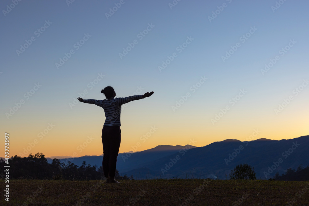 Silhouette of young girl doing yoga in the mountains at sunset sky background