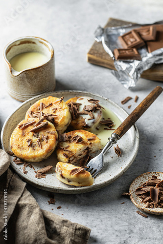 Syrniki or cottage cheese fritters with chocolate poured with condensed milk in the process of eating on ceramics plate