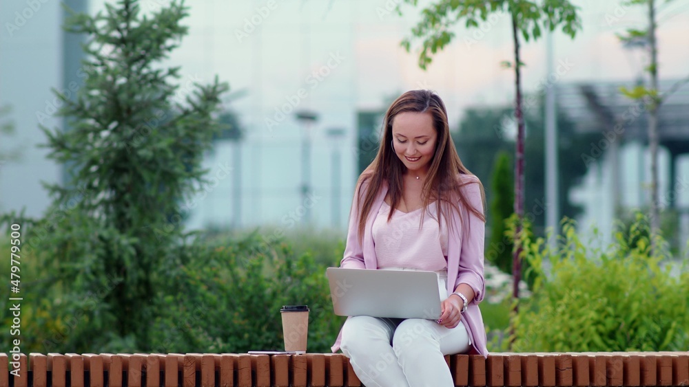 A young woman is sitting at a computer on the street and drinking coffee. Business woman