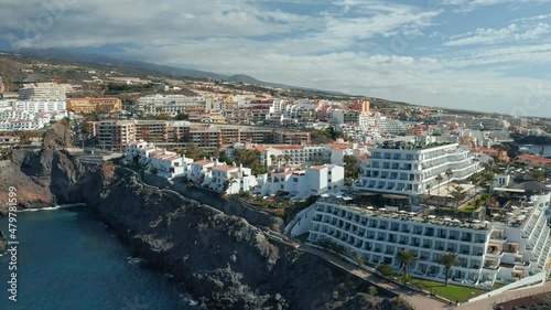 Aerial view of Puerto Santiago city, Tenerife, Canary Islands, Spain. Establishing drone shot of hotels and apartments area in sunny summer day. Bird's eye view of Atlantic ocean coastline