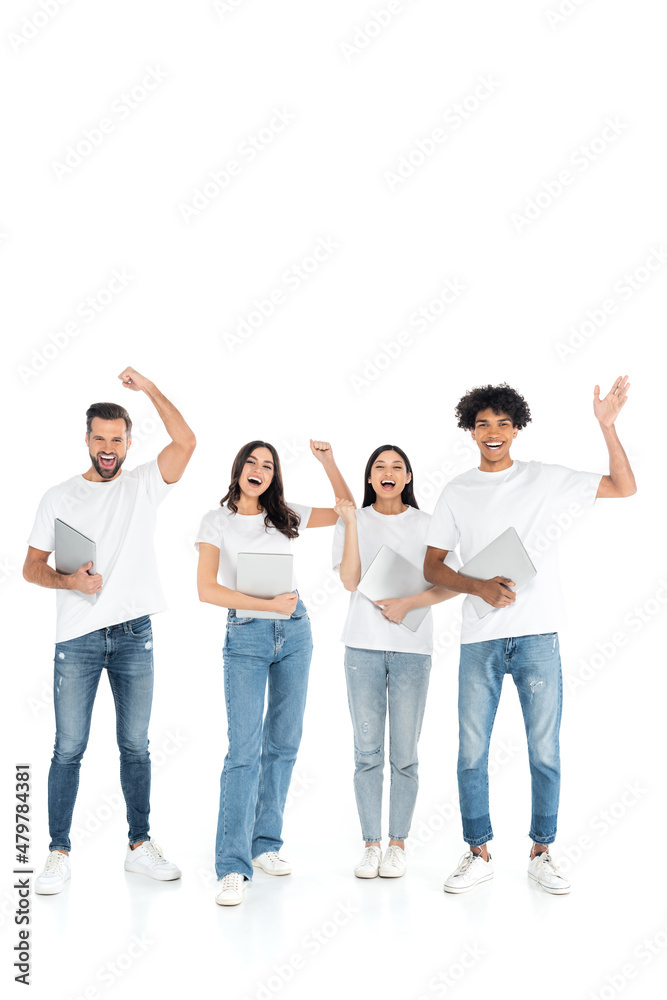 full length view of excited multiethnic friends with laptops showing success gesture on white.