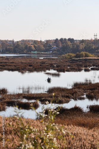 Landscape view of autumn colored river with small boat and fisherman fishing in the middle of river.