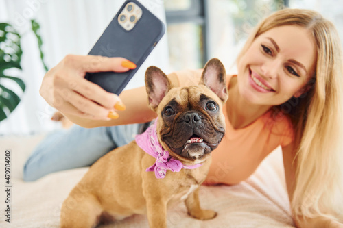 Doing selfie. Woman with pug dog is at home at daytime