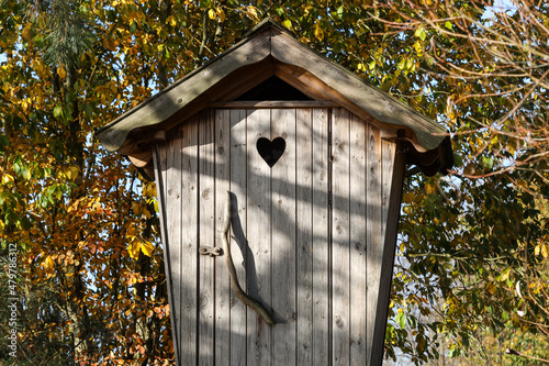 Old countryside wood toilet in autumn conditions with yellow and orange leaves. Decorative heart engraving on the doors. © Artūrs Stiebriņš