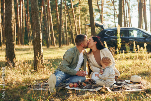 Kissing each other. Happy family of father, mother and little daughter is in the forest