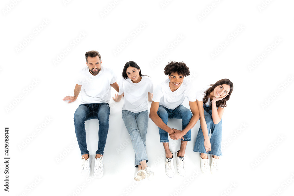 top view of happy multiethnic friends looking at camera while sitting on white. top view of happy multiethnic friends looking at camera while sitting on white.