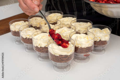 Pastry chef preparing step by step delicious dessert black forest or chip with chocolate biscuit, cream and fresh strawberries in shot glasses