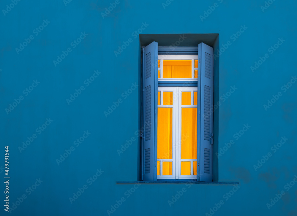 Window at night from outside. Illuminated window with open shutters against blue wall.