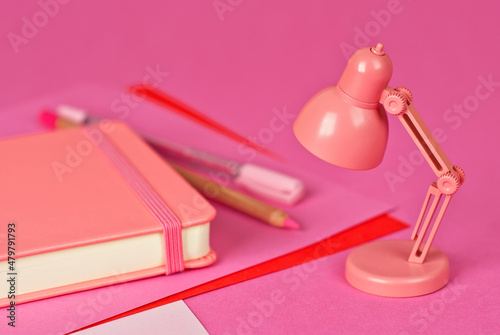 Notepad on a pink background. Toy table lamp near the notebook. Copy space and free space for text near the lamp. The concept of roochy space and creative ideas.