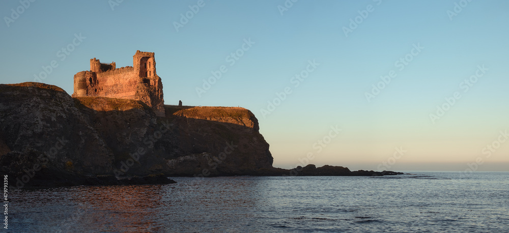 Ruins of an old castle standing on a cliff by the sea at sunset. Scotland 