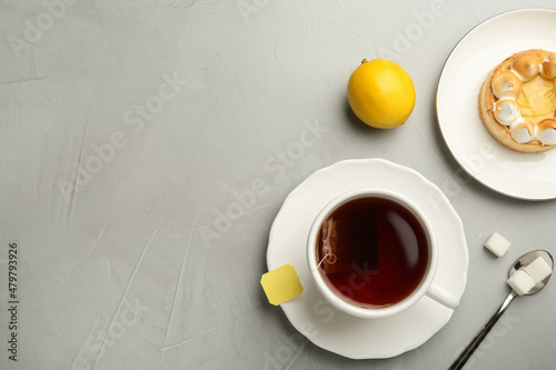 Flat lay composition with tea bag in ceramic cup of hot water and dessert on grey table. Space for text
