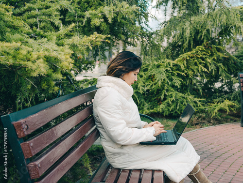 Young woman of Asian appearance searching job with a laptop in an urban park, freelancer. Online communication, online business. The woman blogger works on a laptop computer in the office.