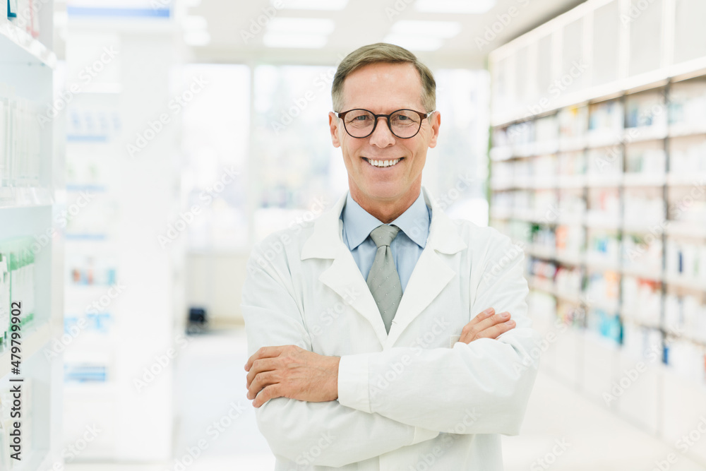 Smiling male caucasian middle-aged mature confident pharmacist druggist in white medical coat standing with arms crossed in pharmacy drugstore