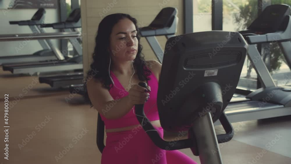 Close-up of a young active sportswoman engaged in a woman in the gym does exercise on a stationary bike, listens to music while doing sports, jogging. Close-up of a young active sportswoman engaged in a woman in the gym does exercise on a stationary bike, listens to music while doing sports, jogging.