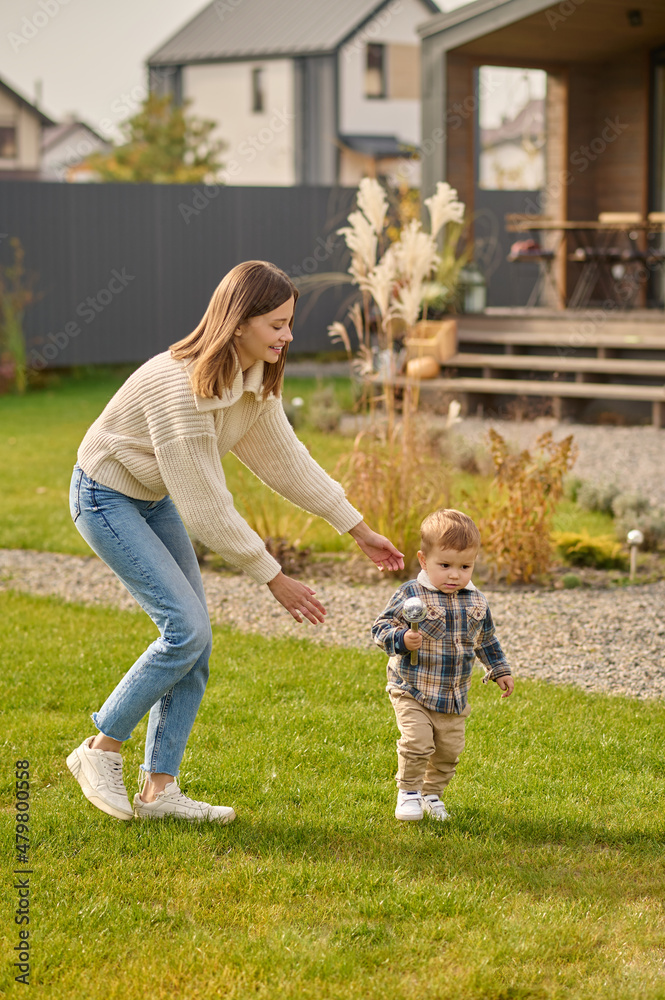 Fototapeta premium Woman playing catching child on green lawn near house