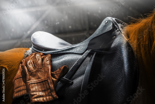 Cowboy gloves and a saddle made of leather on the horse. Horseback equipments for horse riding.